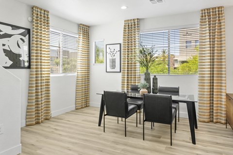 a dining room with a table and chairs and windows with yellow curtains