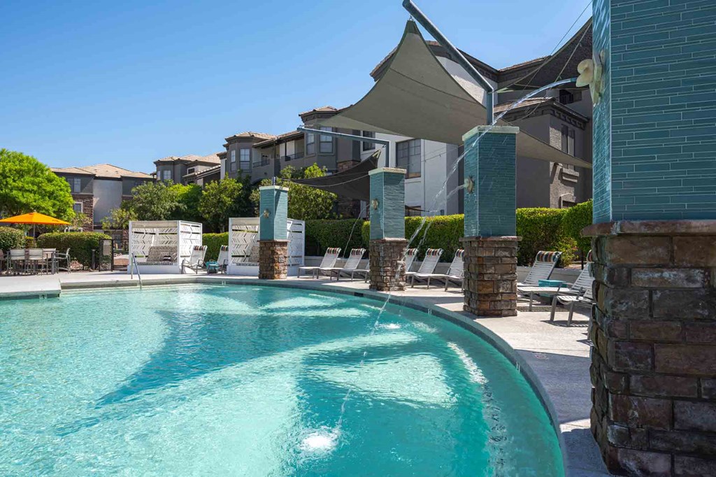 a swimming pool with lounge chairs and umbrellas in front of an apartment building