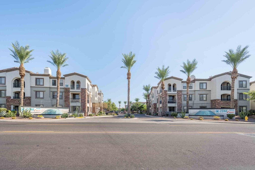 a street view of a row of apartment buildings with palm trees in the background