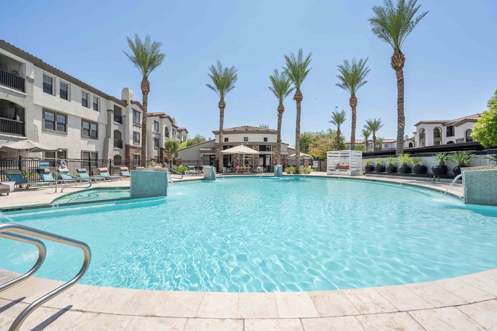Resort-style pool with blue skies, palm trees and the Zone Luxe apartments in Glendale, AZ in the backdrop.