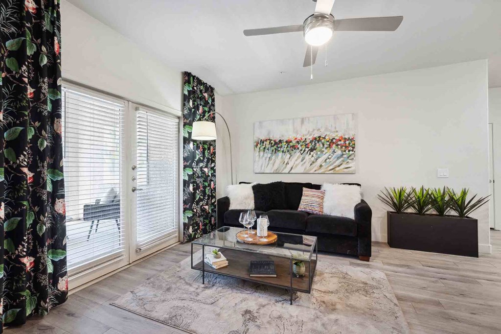 a living room with a black couch and a glass coffee table in front of a sliding glass