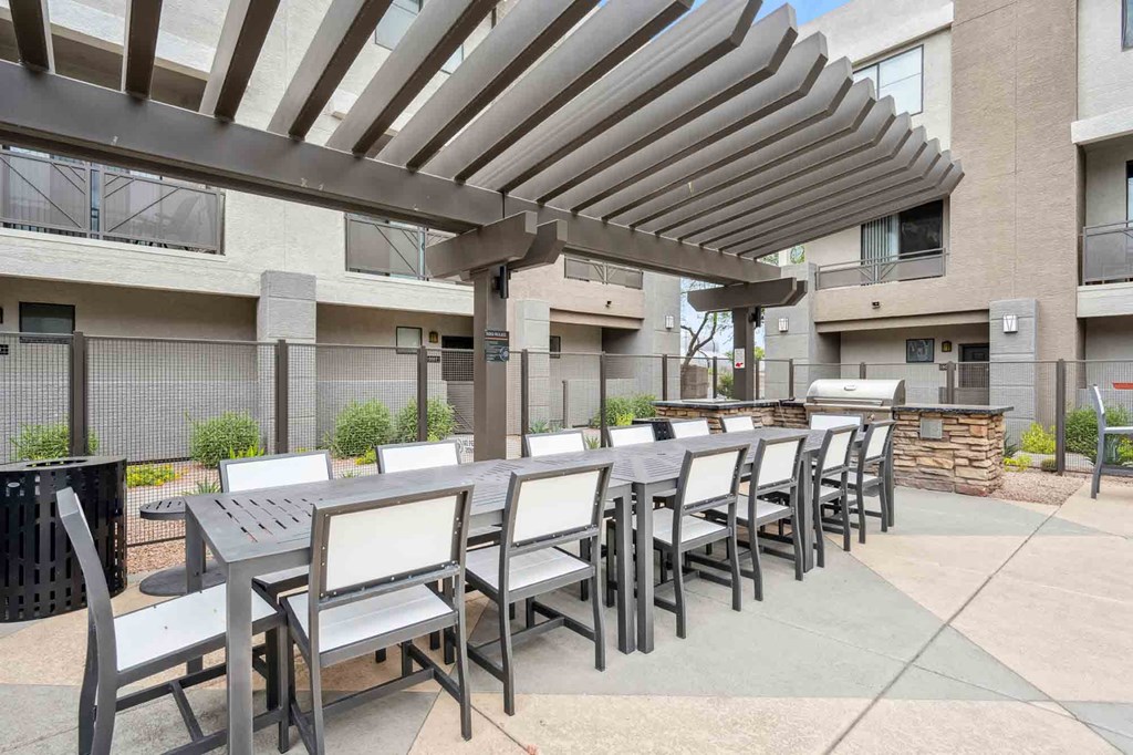 a patio with a long table and chairs and a fire pit in front of a building
