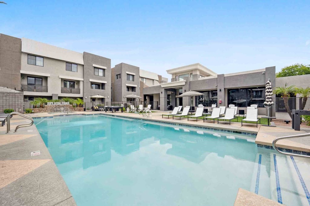 a swimming pool with chaise lounge chairs and umbrellas in front of a building