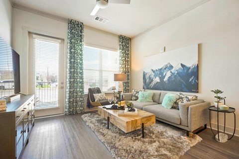 A living room with a grey couch and a large mountain painting on the wall.
