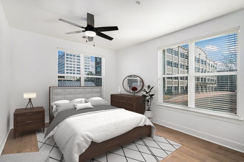 A bedroom with a large bed, a ceiling fan, and a view of a cityscape through the window.