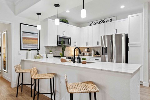 A kitchen with white cabinets and a white island with two barstools.