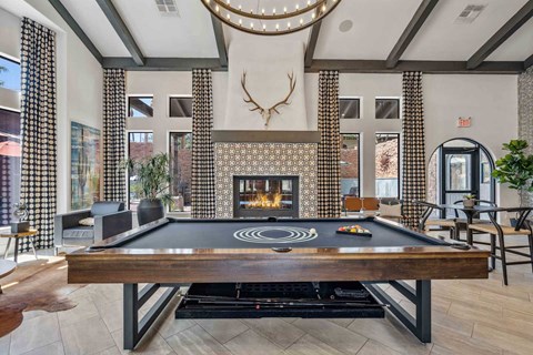 A pool table is in the middle of a room with a fireplace and a deer head mounted on the wall.