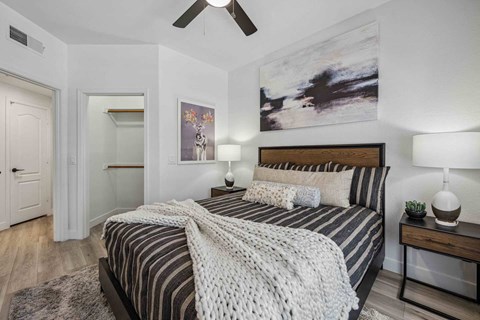 A bedroom with a bed, two lamps, and a painting on the wall.