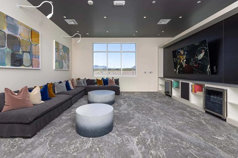 A modern living room with a grey sofa, a grey ottoman, and a large flat screen TV mounted on the wall.