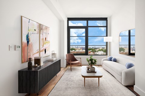 A living room with a large window, a brown chair, a white couch, and a painting on the wall.