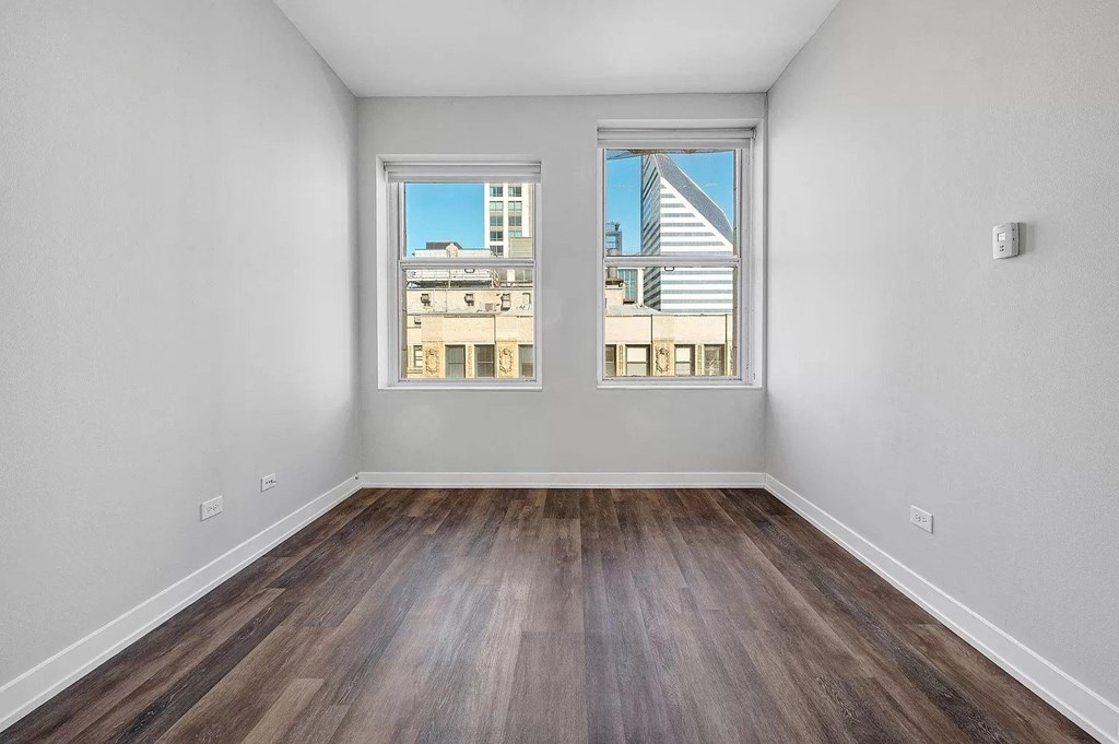 an empty room with two windows and wood floors