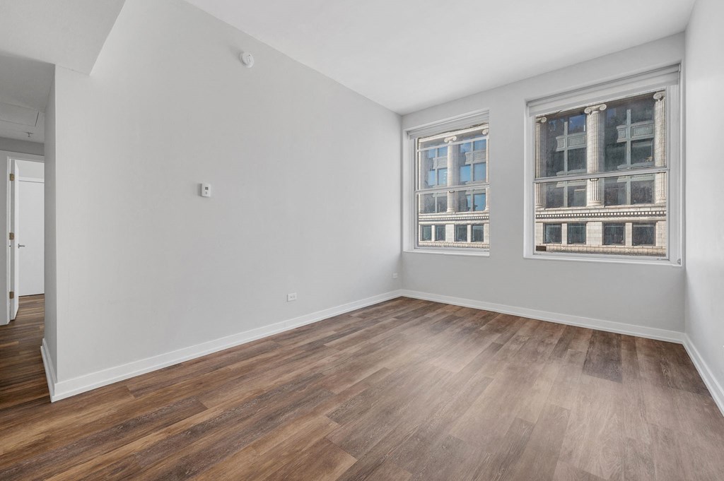 a living room with white walls and wood floors and two windows
