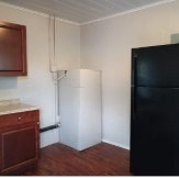 A black refrigerator sits next to a white wall.