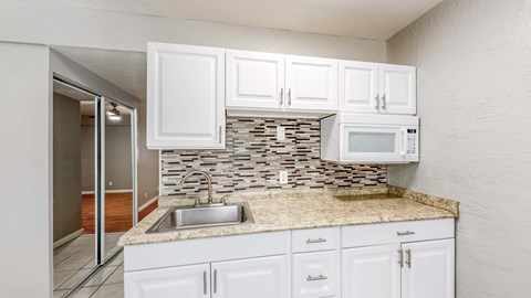 A kitchen with white cabinets and a stone backsplash.