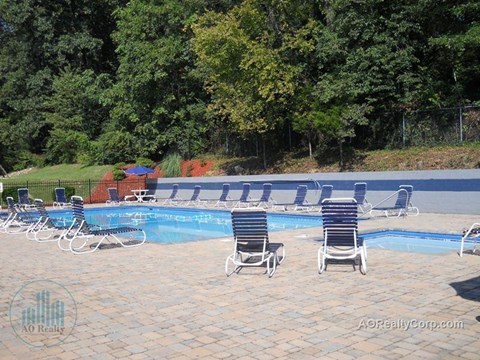 A pool with chairs around it and trees in the background.