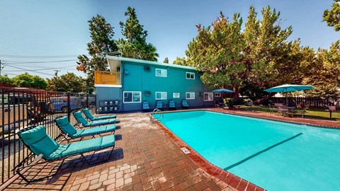 A pool area with a blue building and lounge chairs.