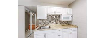 A kitchen with white cabinets and a stone backsplash.