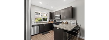 Kitchen with stainless steel appliances, granite counter tops, microwave mounted above stove, window above sink, two barstools at counter, and espresso colored cabinets.