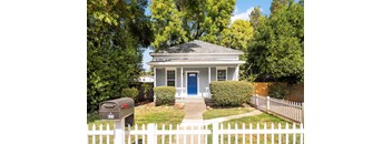 A small house with a blue door is surrounded by a white picket fence.