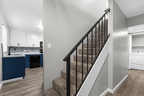 A staircase with a black railing leads to a bedroom with white walls.