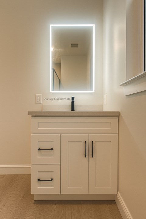 A white cabinet with a mirror above it and a bottle of lotion on the counter.