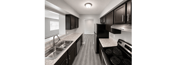 A black and white image of a kitchen with dark cabinets and stainless steel appliances.