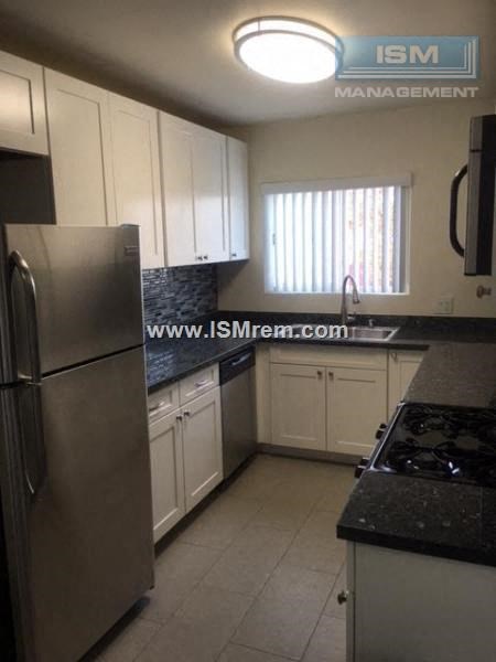 A kitchen with a stainless steel refrigerator and black countertops.