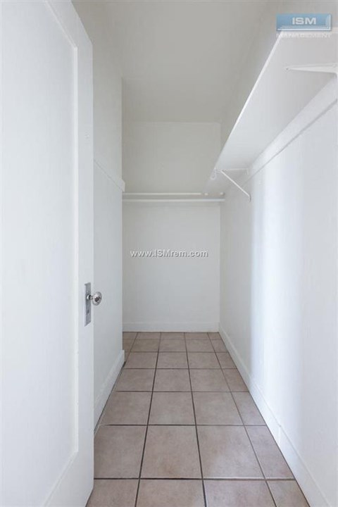 A white hallway with a tiled floor and a door on the left.