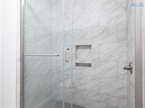A white tiled shower with a glass door and a silver handle.