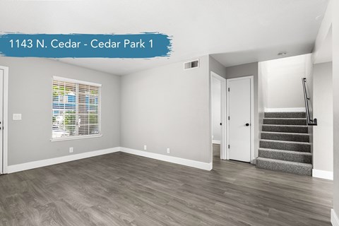 A spacious room with wooden flooring and a staircase leading to another room.
