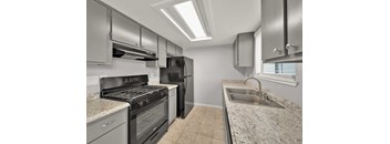 A kitchen with a black stove top oven, black refrigerator, and a granite counter top.