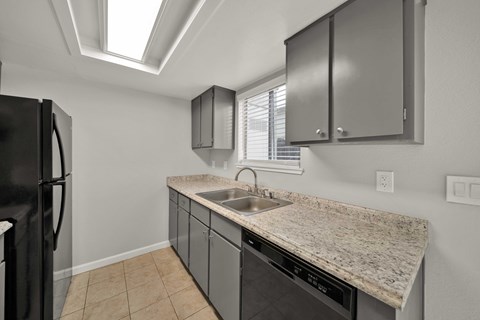 A kitchen with a black refrigerator and a granite countertop.