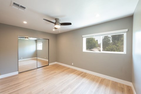 A room with a ceiling fan and a window showing trees outside.