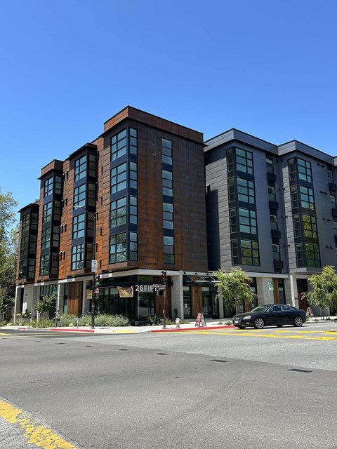 A black car is parked on the side of the road in front of a multi-story building.