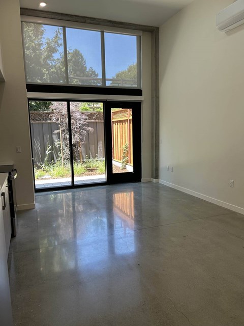 A large empty room with a sliding glass door leading to a backyard.