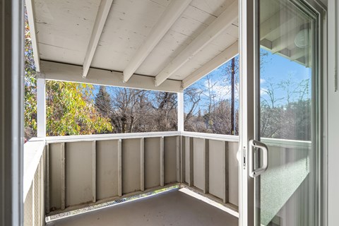 A balcony with a glass door leading to a view of trees.