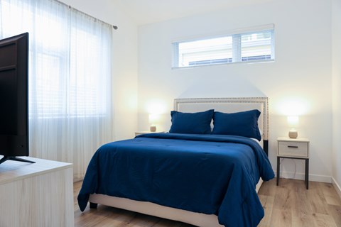 A bedroom with a bed covered in a blue bedspread and two lamps on bedside tables.
