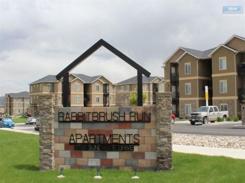 A sign for Rabbitbrush Run Apartments stands in front of a building.