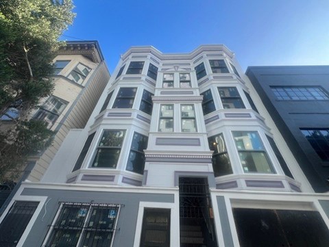 A tall building with a white facade and a balcony on the second floor.