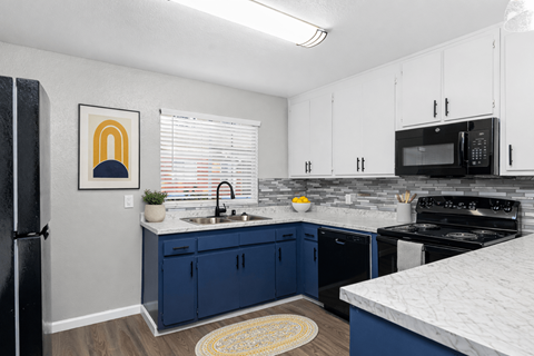 A kitchen with blue cabinets and a black refrigerator.
