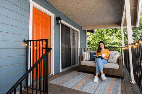 A woman is sitting on a couch on a porch with a book in her hands.