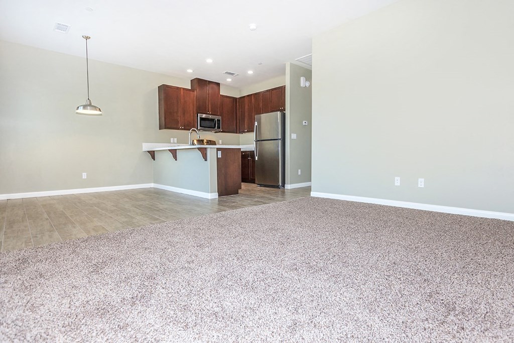 an empty living room with a kitchen with stainless steel appliances