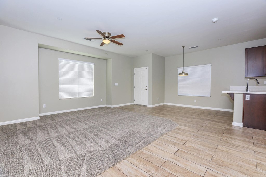 an empty living room with a ceiling fan and a kitchen
