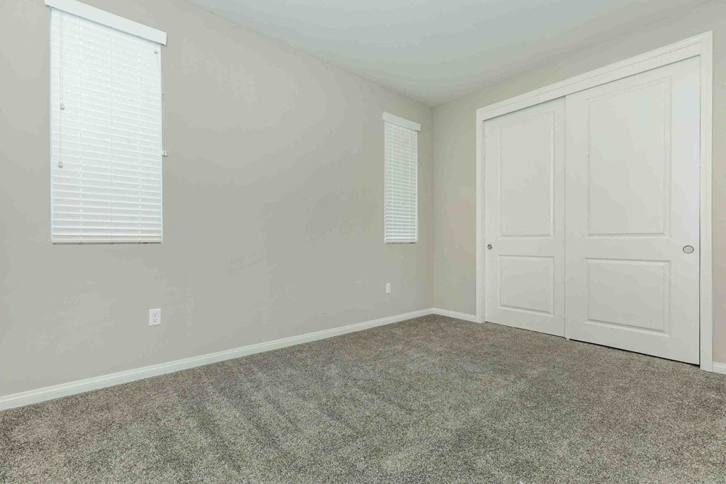 an empty bedroom with white doors and a carpeted floor