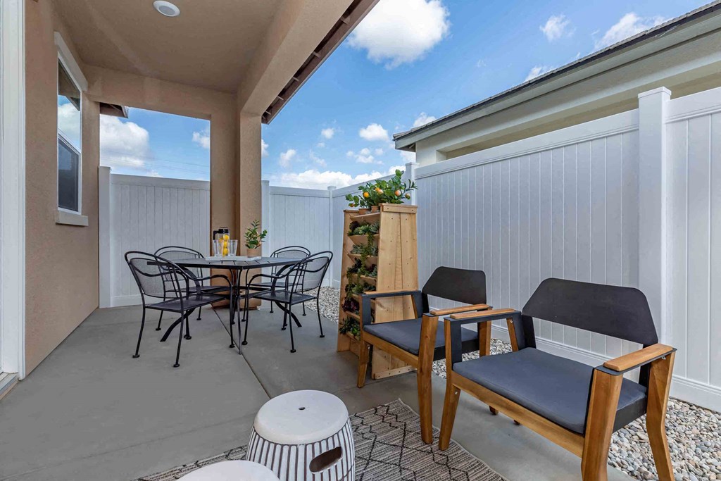 a patio with a table and chairs next to a white fence