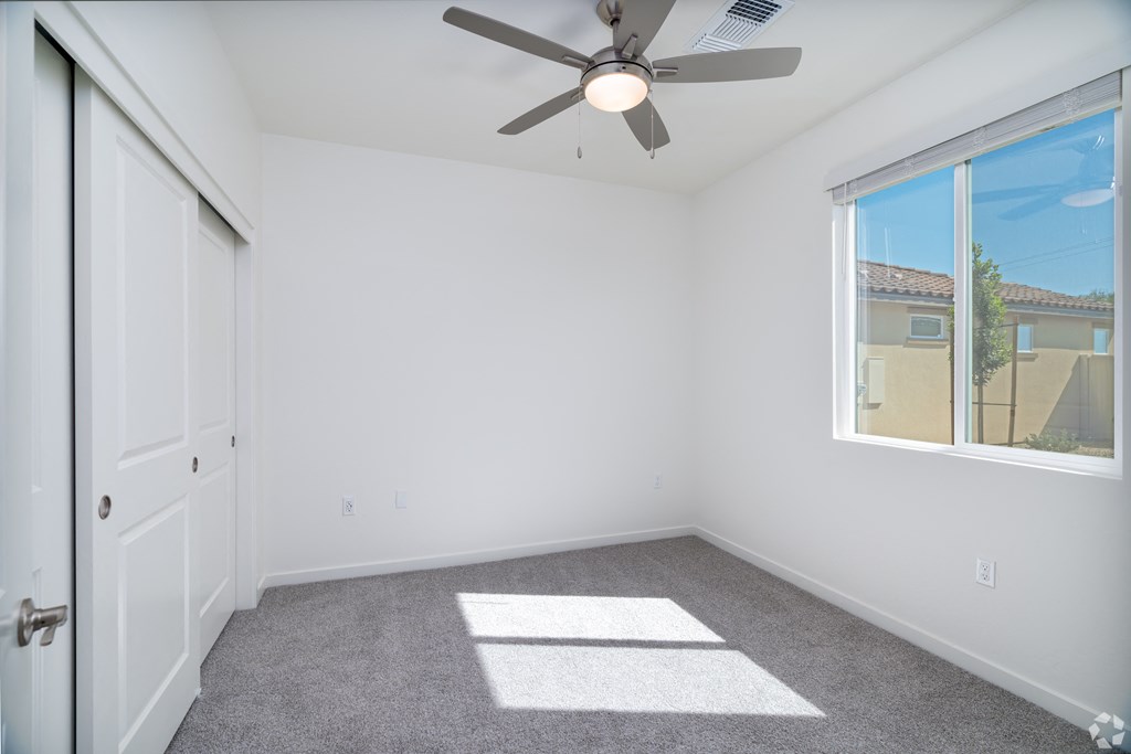 an empty bedroom with a ceiling fan and a window