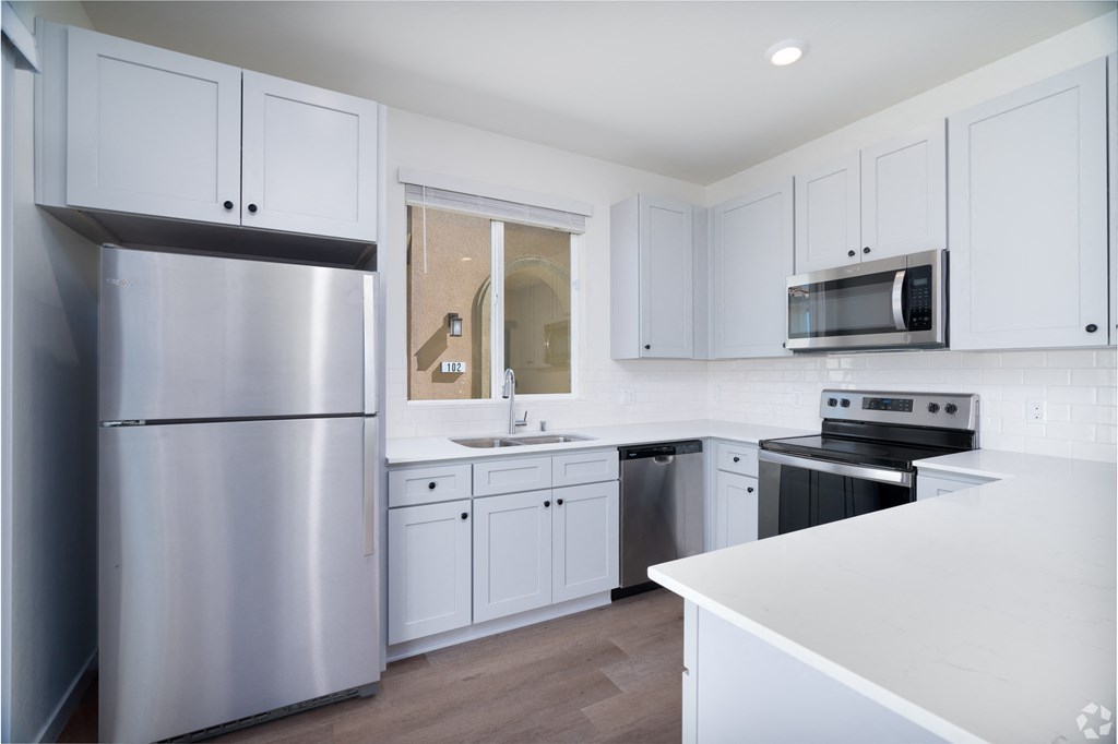 a white kitchen with stainless steel appliances and gray cabinets