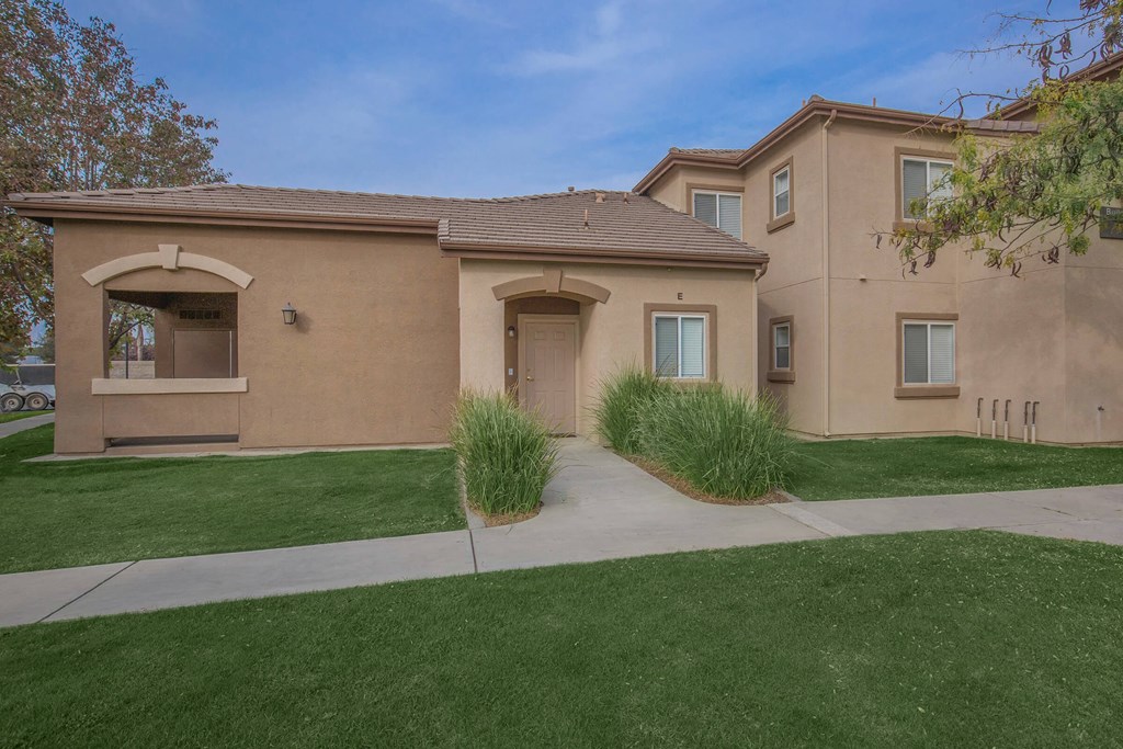 the front of a tan house with a sidewalk and grass