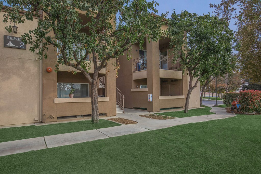 a tan apartment building with trees and a sidewalk