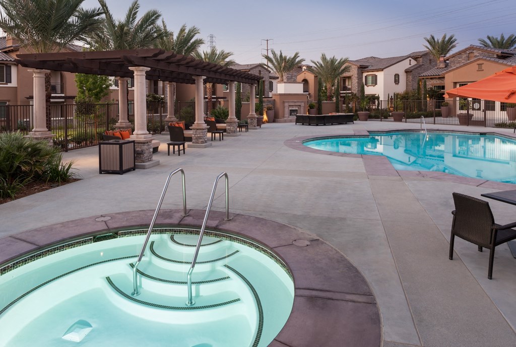 a resort style swimming pool and spa with chairs and umbrellas